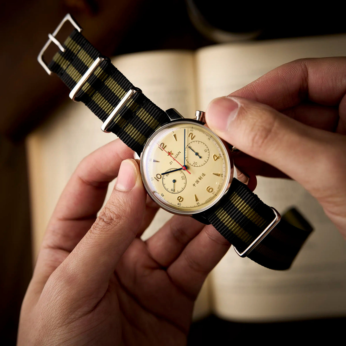 Seagull 1963 Air Force Cream 42mm held in both hands over an open book, dial angled to the light