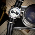 Seagull 1963 White Panda Sport 42mm from above on its striped nylon strap beside a camera lens