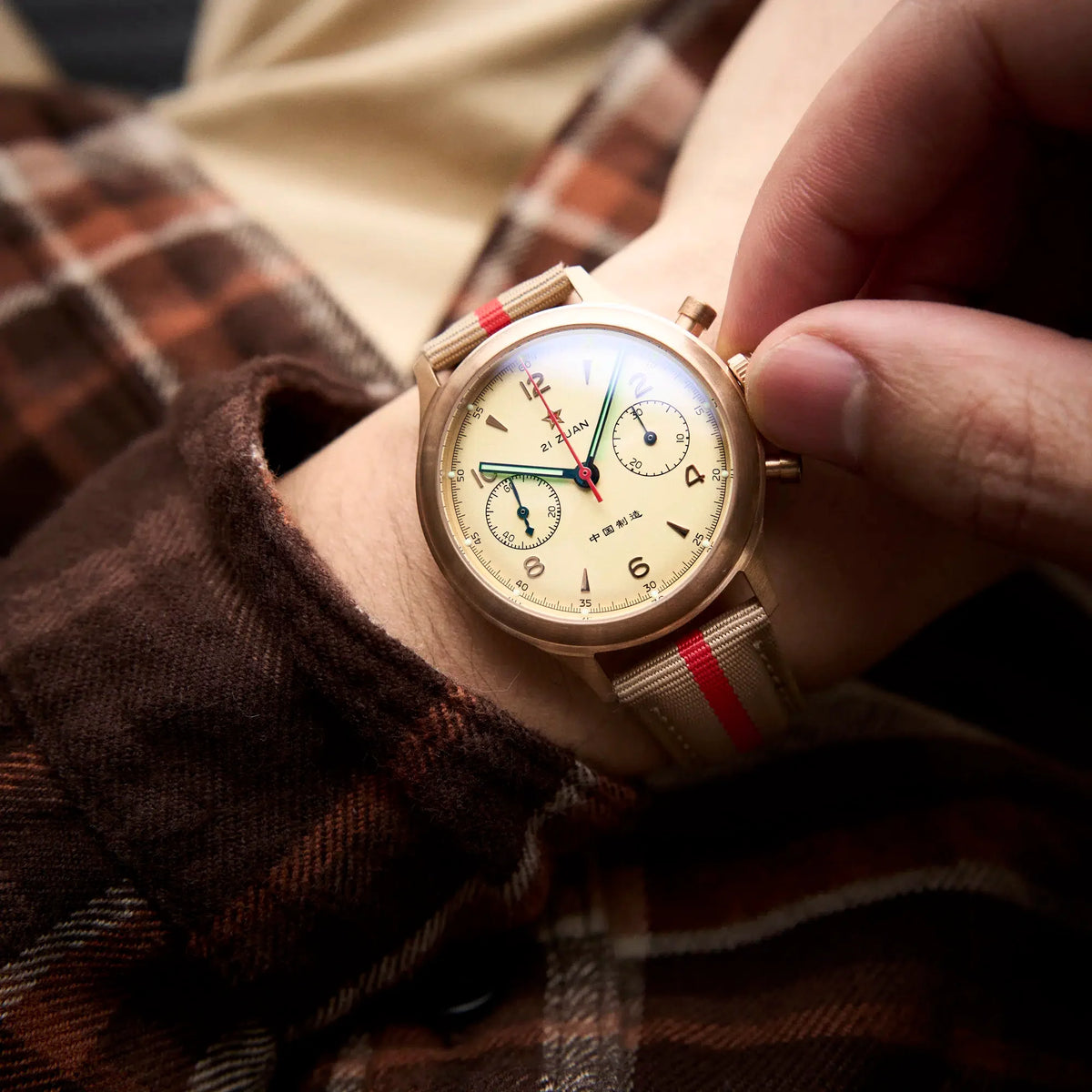 Seagull 1963 Bronze Lume on the wrist with a brown plaid flannel cuff, fingers on the crown
