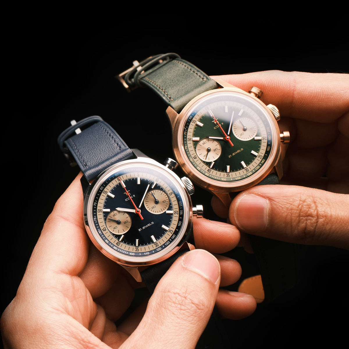 Seagull 1963 Icon II Blue held in front of the green bronze version against a black background