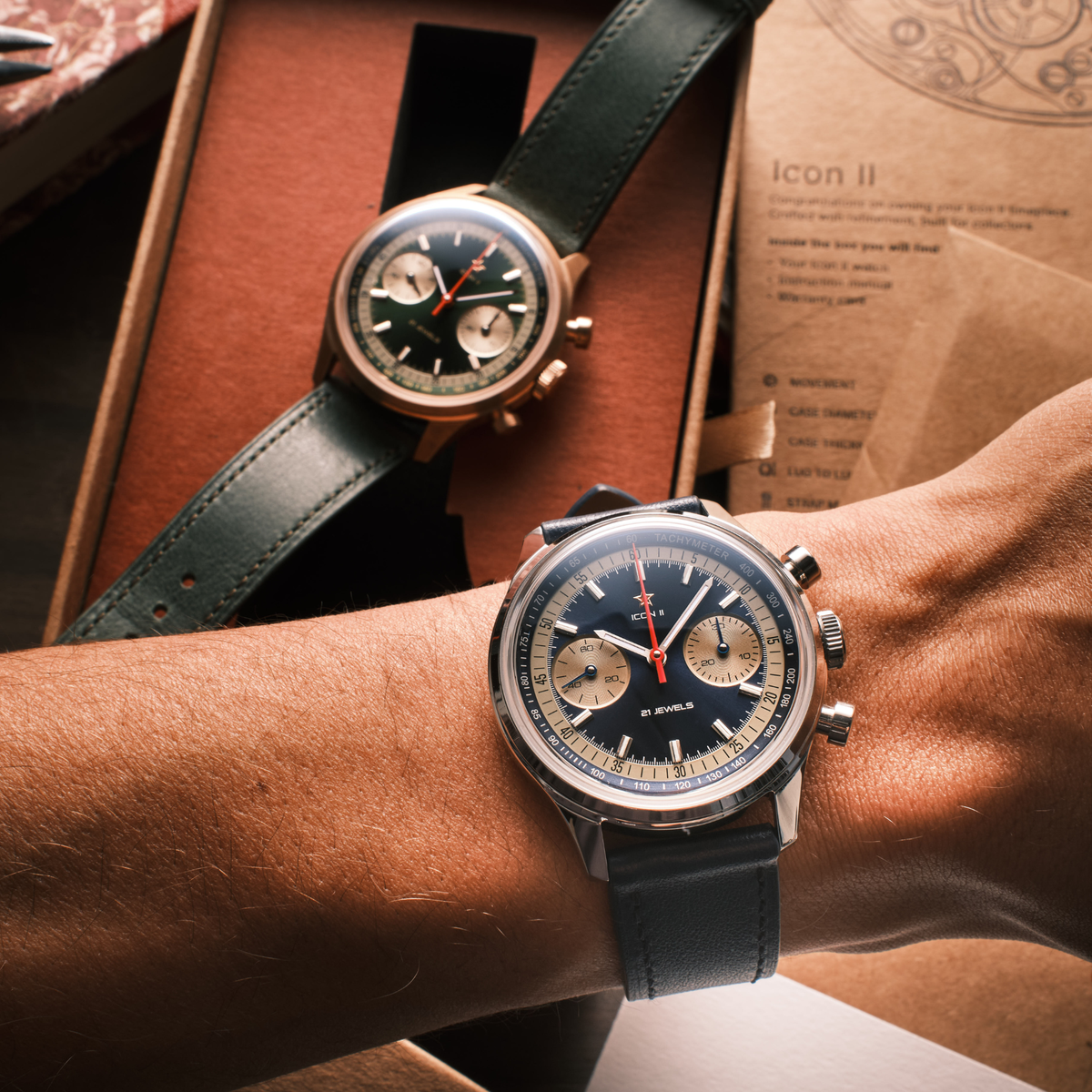 Seagull 1963 Icon II Blue worn on the wrist with the green bronze version open in its box behind
